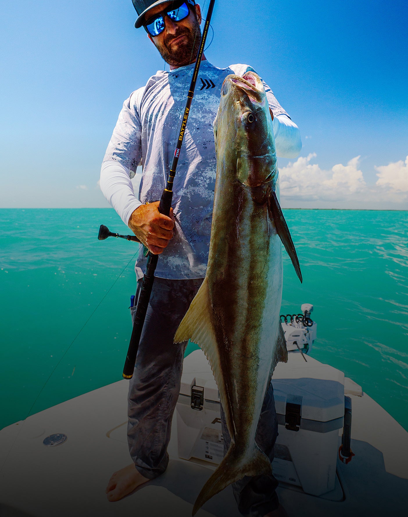 Man holding a large fish on a boat with clear blue water and sky in the background
