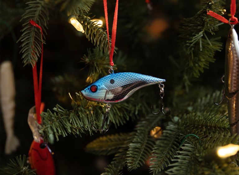 Decorative fishing lure ornament on a Christmas tree with blurred lights in the background.