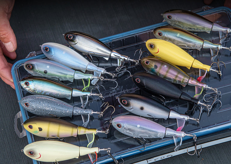 A collection of Screamin Choppo Baits in an arrangement of colors laying flat on a Plano Tackle Box.
