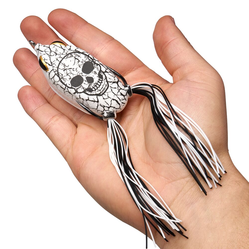 A hand holding a white and black fishing lure with a skull design and black-and-white silicone strands.
