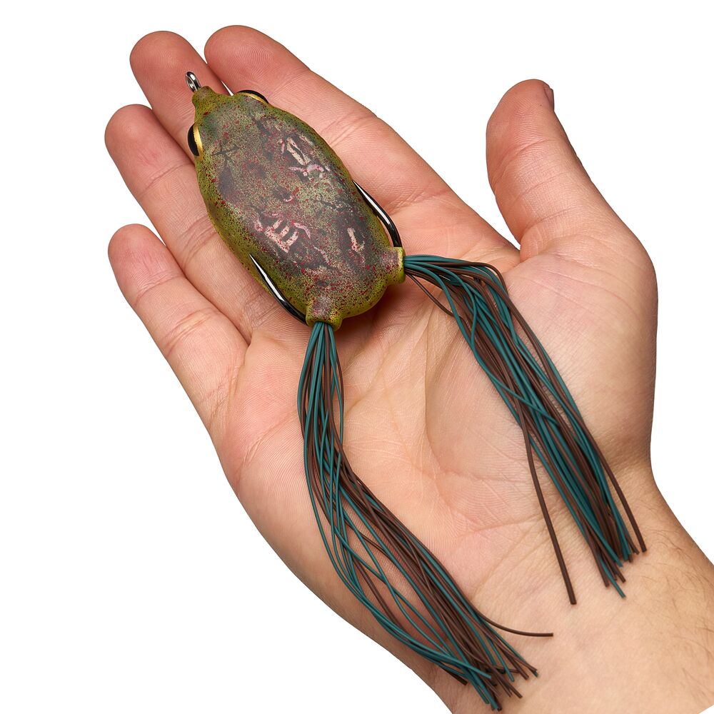 A fishing lure with a textured olive-green and brown body and two dark teal skirt strands, held in a person's hand against a white background.