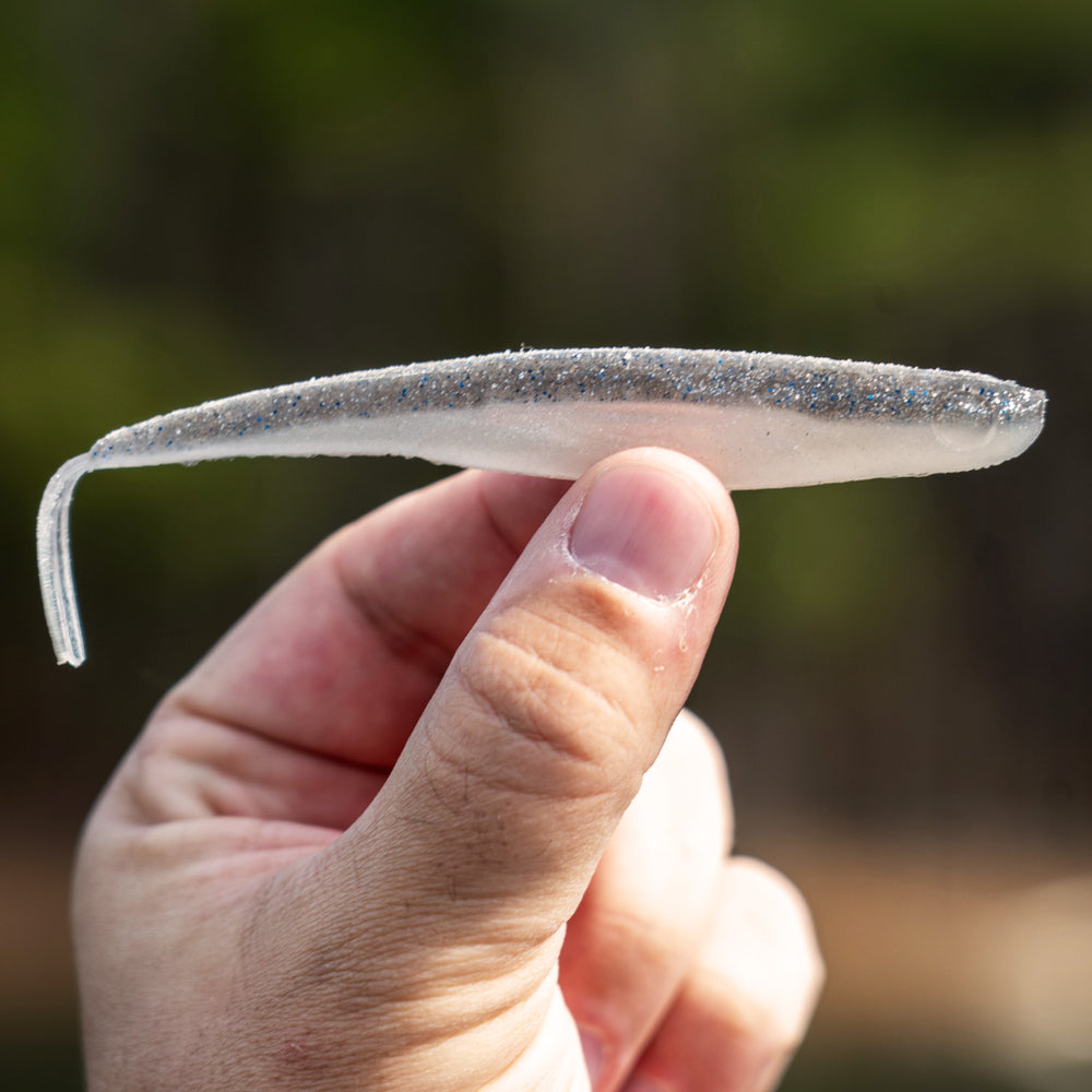 Hand holding a small, flat, metallic object against a blurred natural background